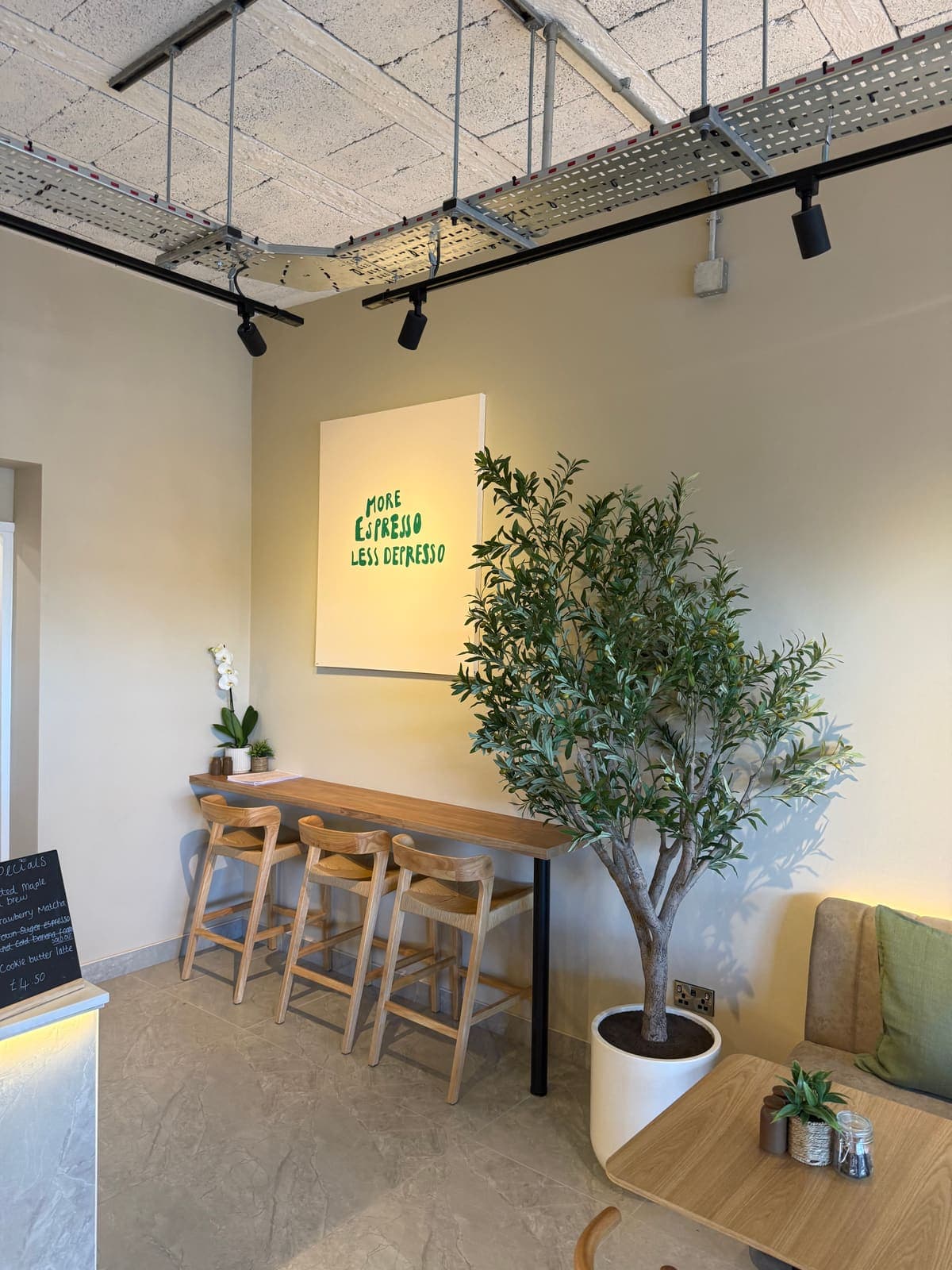 High table and stools beside an olive tree inside TOAST & Co café in Allestree, Derby