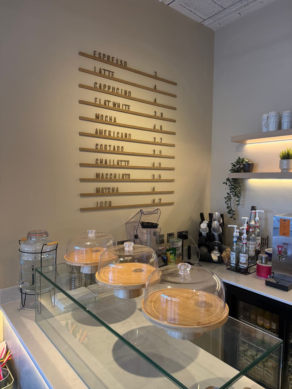 The coffee menu board and glass cake domes on the counter at TOAST & Co in Allestree, Derby