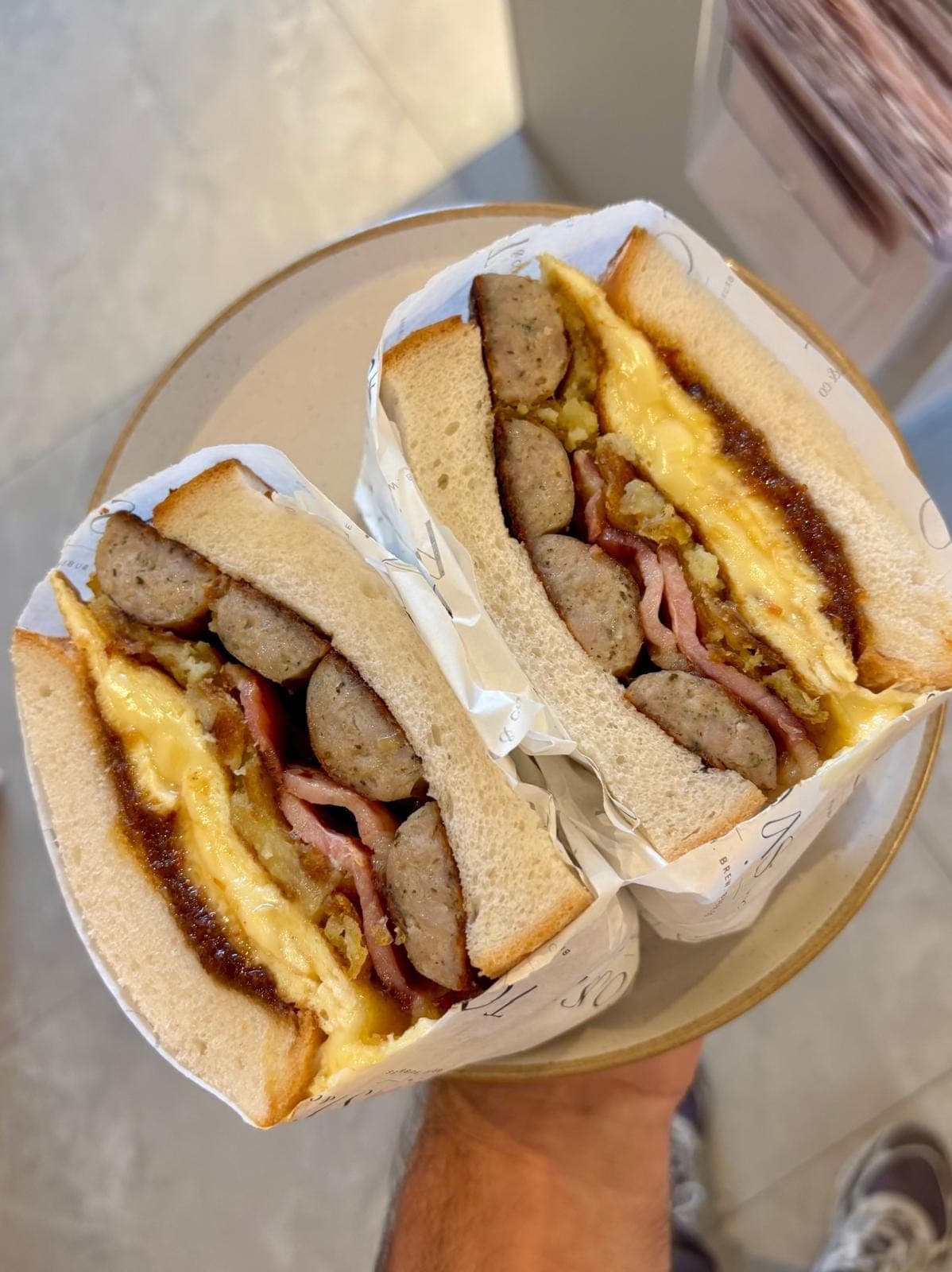 Brunch Sandwich halves wrapped in TOAST & Co paper, filled with pork sausage, bacon, scrambled omelette and hashed potato